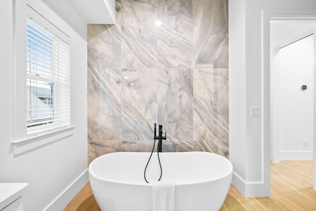 full bathroom with a freestanding tub, baseboards, wood finished floors, and tile walls