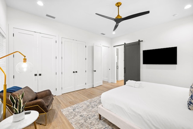 bedroom with a barn door, light wood-style flooring, visible vents, two closets, and recessed lighting