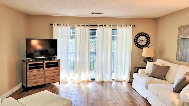 living area featuring wood finish floors, a textured ceiling, baseboards, and visible vents
