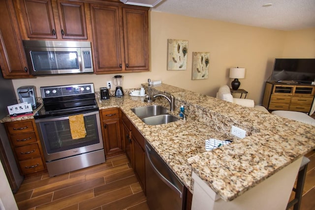 kitchen with a peninsula, light stone countertops, appliances with stainless steel finishes, wood tiled floor, and a sink