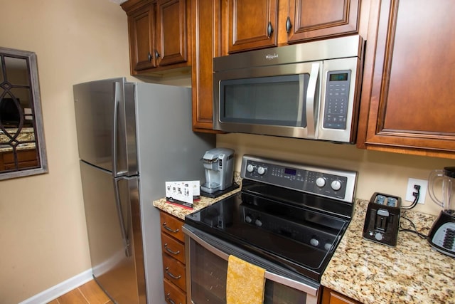 kitchen featuring baseboards, light stone countertops, brown cabinets, wood finished floors, and appliances with stainless steel finishes