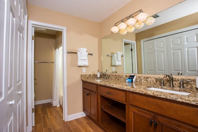 full bath featuring double vanity, a textured ceiling, a sink, and wood finish floors
