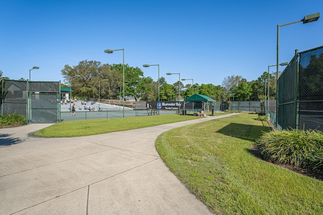 view of property's community featuring a lawn, fence, and a tennis court