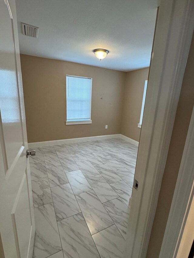 empty room with marble finish floor, a textured ceiling, baseboards, and visible vents