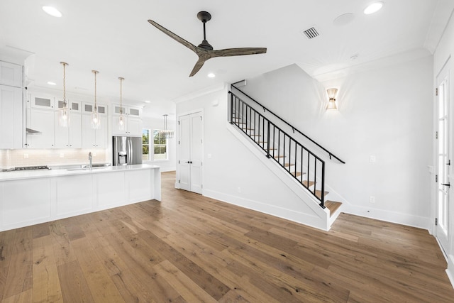 unfurnished living room featuring hardwood / wood-style floors, stairs, crown molding, and a ceiling fan