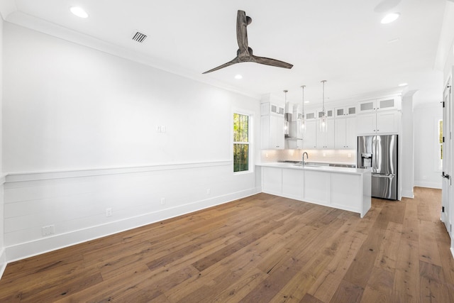 kitchen with visible vents, crown molding, a peninsula, wall chimney exhaust hood, and stainless steel refrigerator with ice dispenser