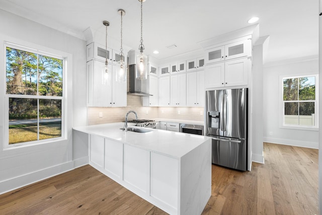kitchen with wood finished floors, appliances with stainless steel finishes, a peninsula, wall chimney range hood, and decorative backsplash