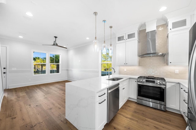 kitchen with a peninsula, wall chimney exhaust hood, stainless steel appliances, a sink, and hardwood / wood-style floors
