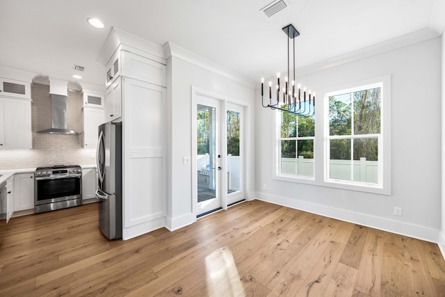 kitchen featuring crown molding, backsplash, wall chimney exhaust hood, stainless steel appliances, and visible vents