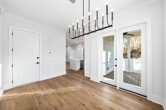 unfurnished dining area with a notable chandelier, ornamental molding, baseboards, and light wood-type flooring