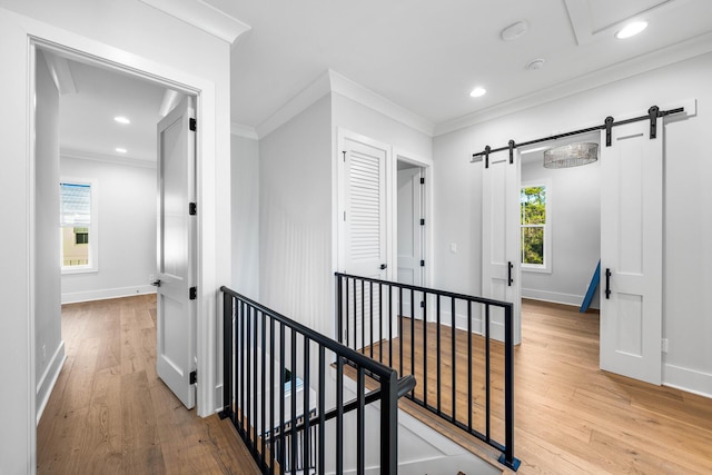 hallway with a barn door, wood finished floors, crown molding, and an upstairs landing