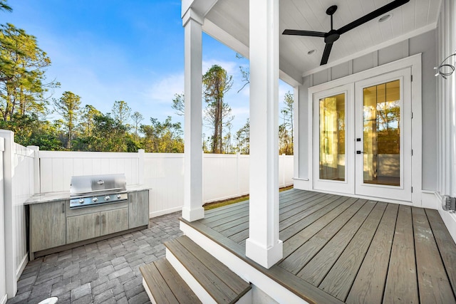 deck featuring ceiling fan, a fenced backyard, a grill, french doors, and an outdoor kitchen