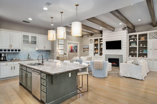 kitchen with white cabinets, visible vents, light wood-style flooring, a kitchen island with sink, and a sink