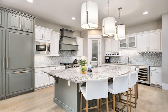 kitchen featuring built in appliances, a breakfast bar area, a center island with sink, beverage cooler, and custom exhaust hood