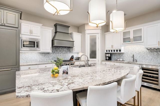kitchen featuring decorative backsplash, custom exhaust hood, a sink, beverage cooler, and built in appliances