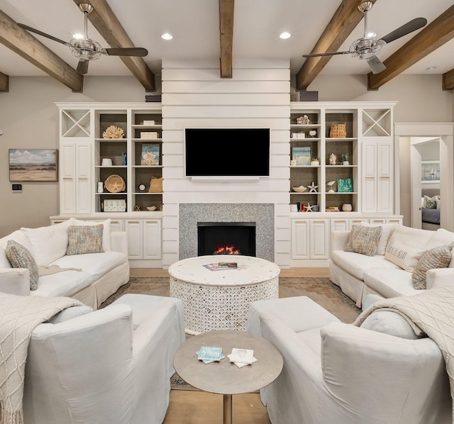 living area featuring a lit fireplace, a ceiling fan, beamed ceiling, light wood-style floors, and recessed lighting