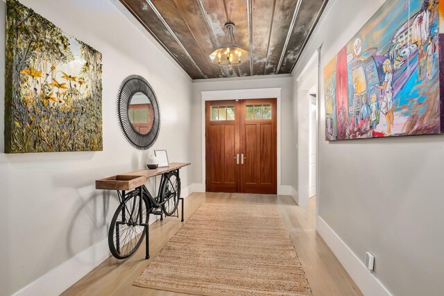 foyer with an inviting chandelier, wood ceiling, baseboards, and light wood finished floors