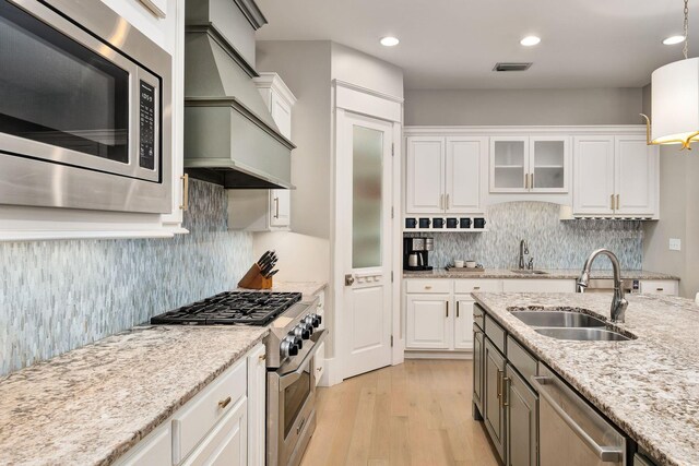 kitchen with premium range hood, white cabinets, a sink, and stainless steel appliances