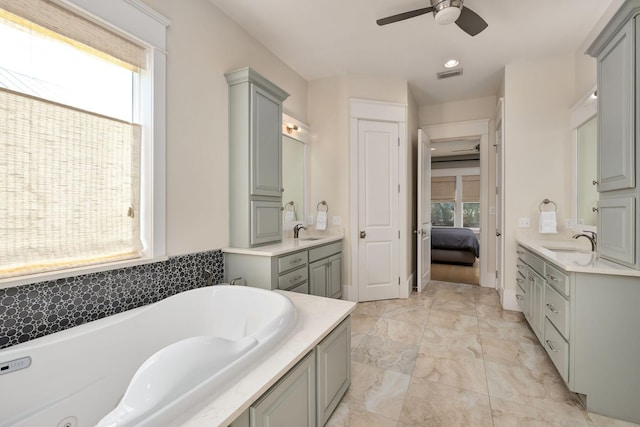 ensuite bathroom with visible vents, a bath, a sink, and a ceiling fan