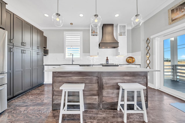 kitchen with a kitchen breakfast bar, crown molding, a sink, light countertops, and custom exhaust hood