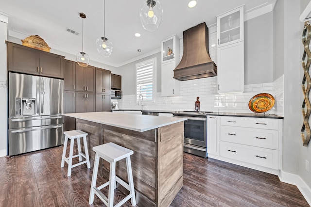 kitchen with appliances with stainless steel finishes, visible vents, a kitchen island, premium range hood, and dark wood-type flooring