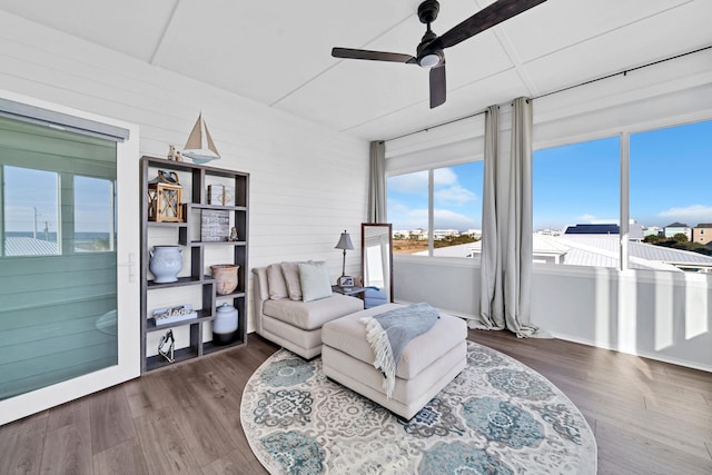 living area with a ceiling fan, wood walls, and wood finished floors