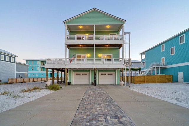 raised beach house with a garage, fence, a balcony, and driveway
