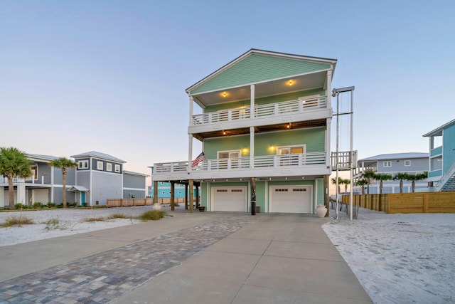 coastal inspired home featuring fence, concrete driveway, a balcony, and a garage