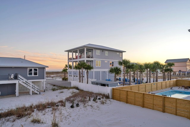 back of house at dusk featuring a fenced backyard, an outdoor pool, and stairs