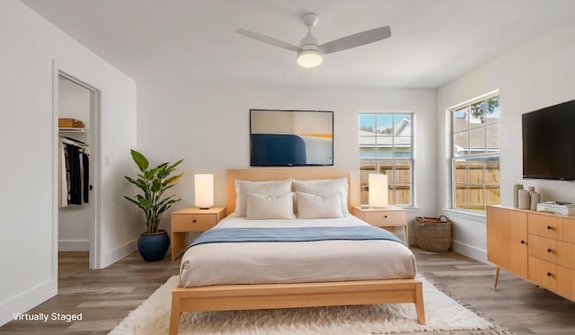 bedroom with baseboards, a spacious closet, a ceiling fan, and light wood-style flooring