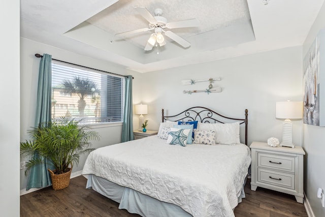 bedroom featuring a ceiling fan, a raised ceiling, dark wood-style floors, and baseboards