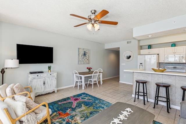 living area with a textured ceiling, visible vents, baseboards, ceiling fan, and light tile patterned floors