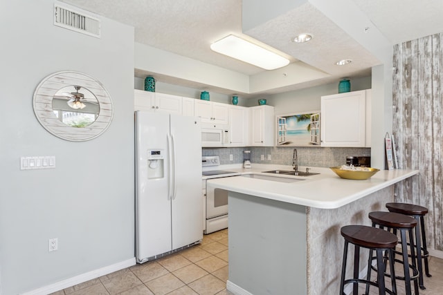 kitchen featuring a breakfast bar area, white appliances, a sink, visible vents, and a peninsula