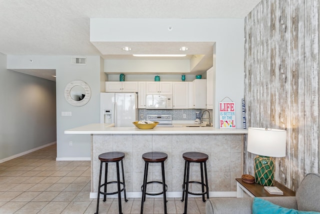 kitchen featuring visible vents, a kitchen breakfast bar, a peninsula, white appliances, and backsplash