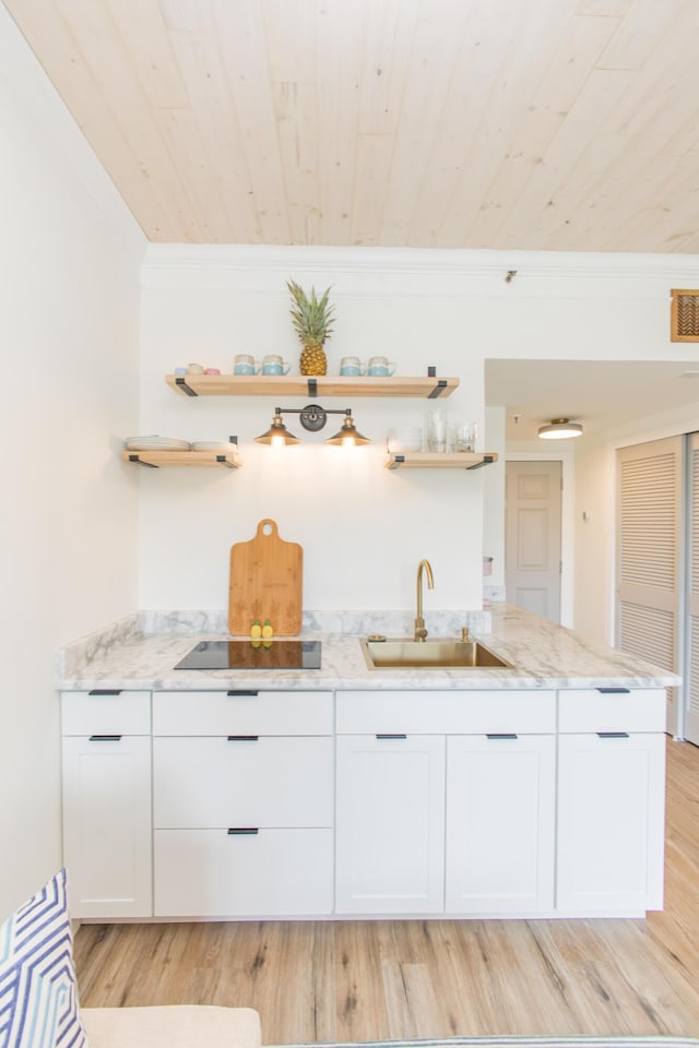 bar featuring black electric cooktop, a sink, indoor wet bar, light wood finished floors, and ornamental molding