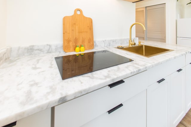 kitchen featuring freestanding refrigerator, white cabinetry, black electric cooktop, light stone counters, and a sink