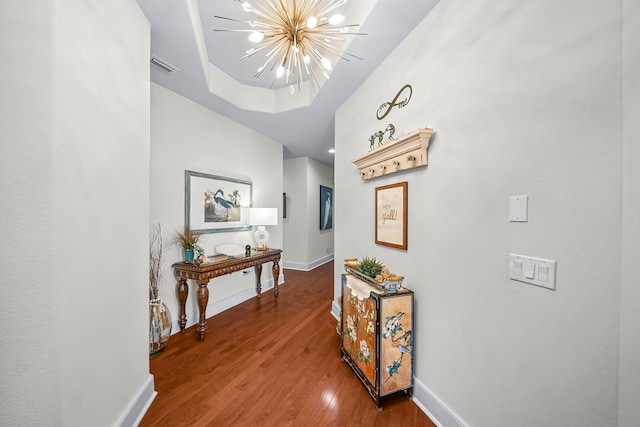 hall featuring baseboards, wood finished floors, a chandelier, and visible vents