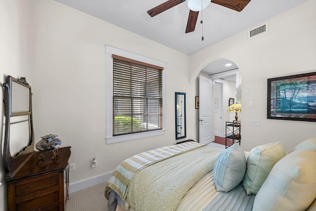 carpeted bedroom with arched walkways, baseboards, visible vents, and a ceiling fan