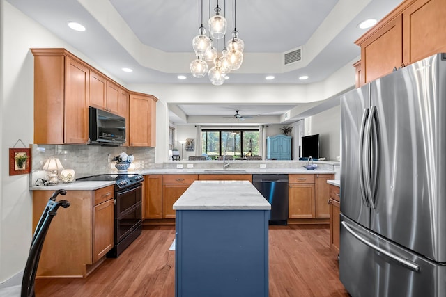 kitchen with a sink, a center island, a peninsula, a tray ceiling, and black appliances