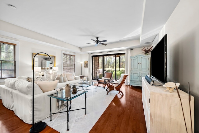 living area featuring ceiling fan, a tray ceiling, wood finished floors, and visible vents