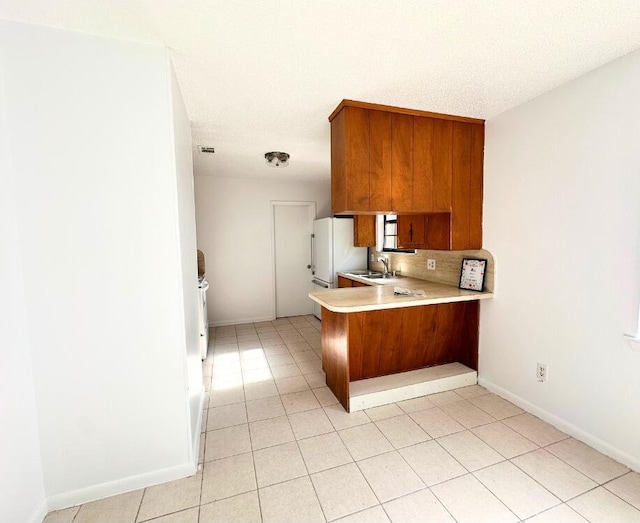 102 Alice Dr, Defuniak Springs, FL 32435 - kitchen featuring a sink, light countertops, a peninsula, brown cabinetry, and decorative backsplash