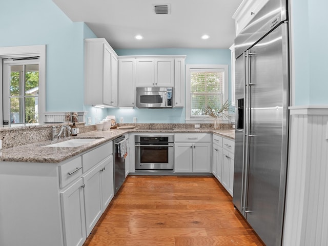 253 Salt Box Ln, Watersound, FL 32461 - kitchen with stainless steel appliances, a sink, white cabinetry, light stone counters, and light wood finished floors