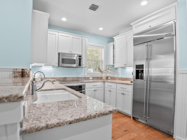 253 Salt Box Ln, Watersound, FL 32461 - kitchen with appliances with stainless steel finishes, a sink, white cabinetry, light stone countertops, and light wood-type flooring