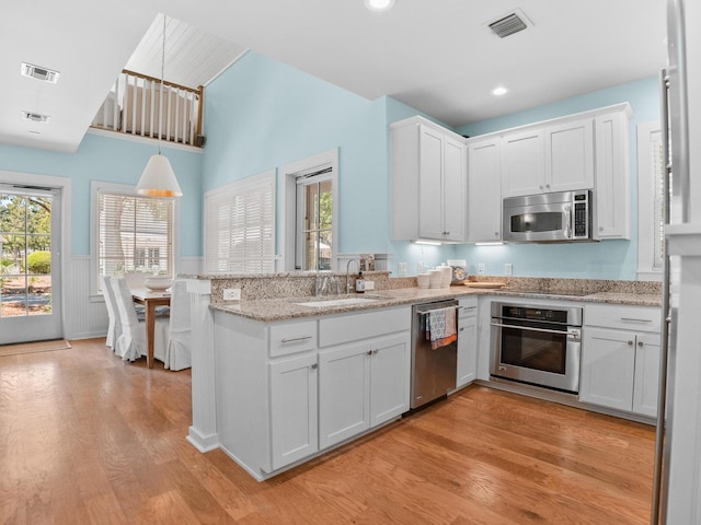 253 Salt Box Ln, Watersound, FL 32461 - kitchen with stainless steel appliances, a sink, a peninsula, a wainscoted wall, and light wood-type flooring