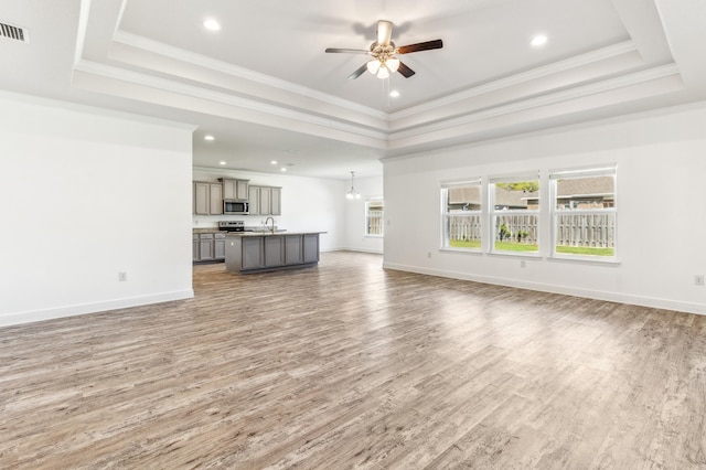 unfurnished living room with ceiling fan, a sink, a raised ceiling, baseboards, and wood finished floors