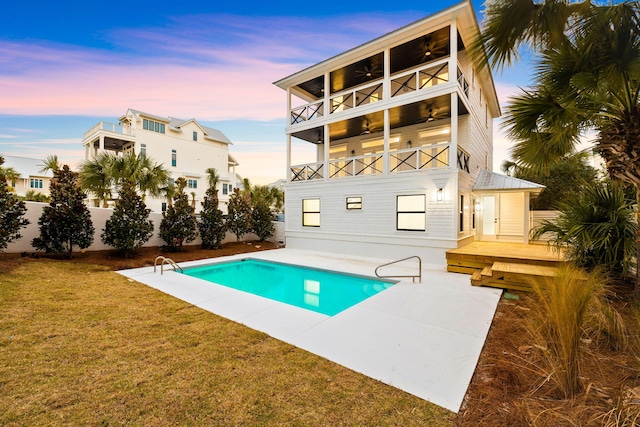 pool at dusk featuring a fenced in pool, fence, a patio, a lawn, and ceiling fan