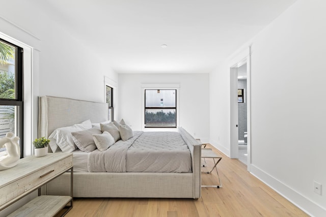 bedroom with ensuite bathroom, multiple windows, light wood-style floors, and baseboards