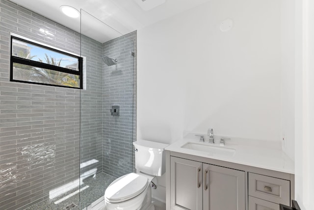 full bathroom featuring a tile shower, toilet, and vanity