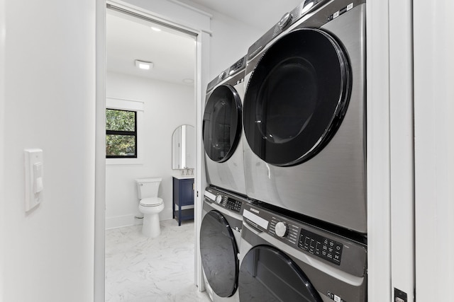 laundry room featuring marble finish floor, baseboards, laundry area, and stacked washer / drying machine