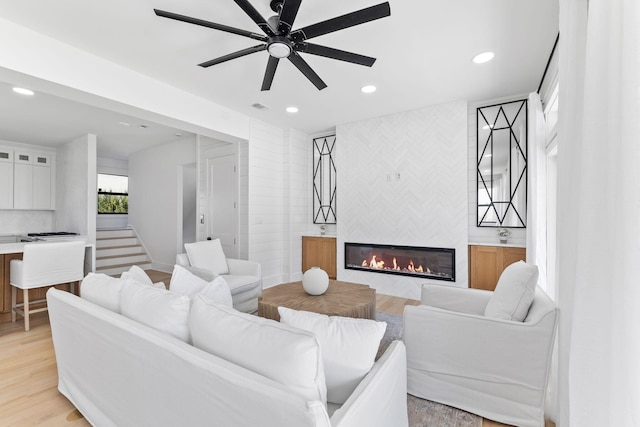 living room with visible vents, ceiling fan, recessed lighting, a tiled fireplace, and light wood-style floors